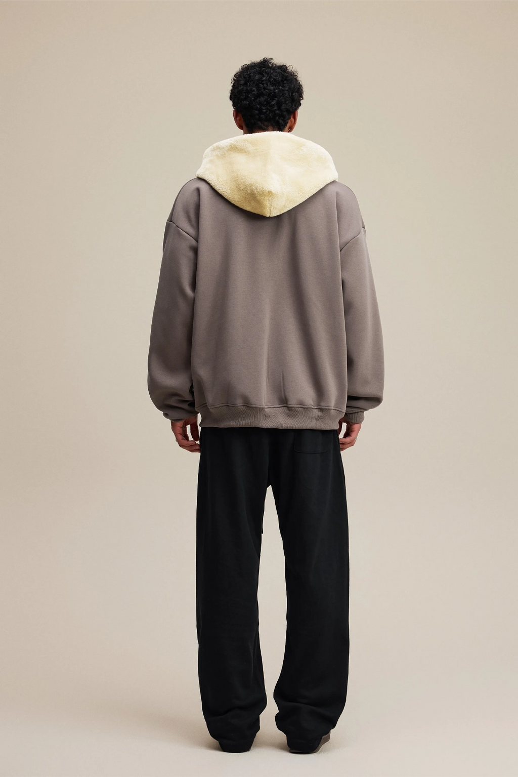 Person wearing a gray hoodie with a light-colored hood on a beige background