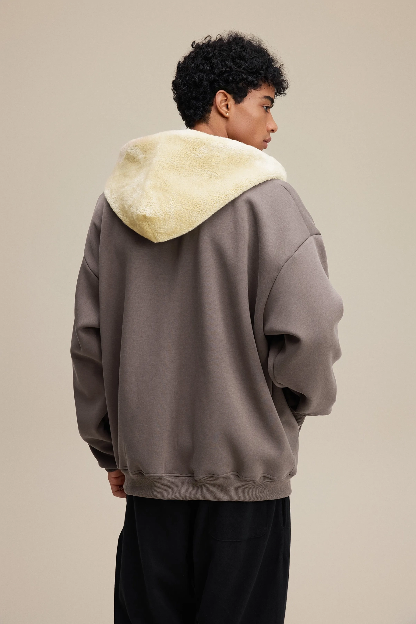 Person wearing a gray hoodie with a cream-colored hood against a beige background