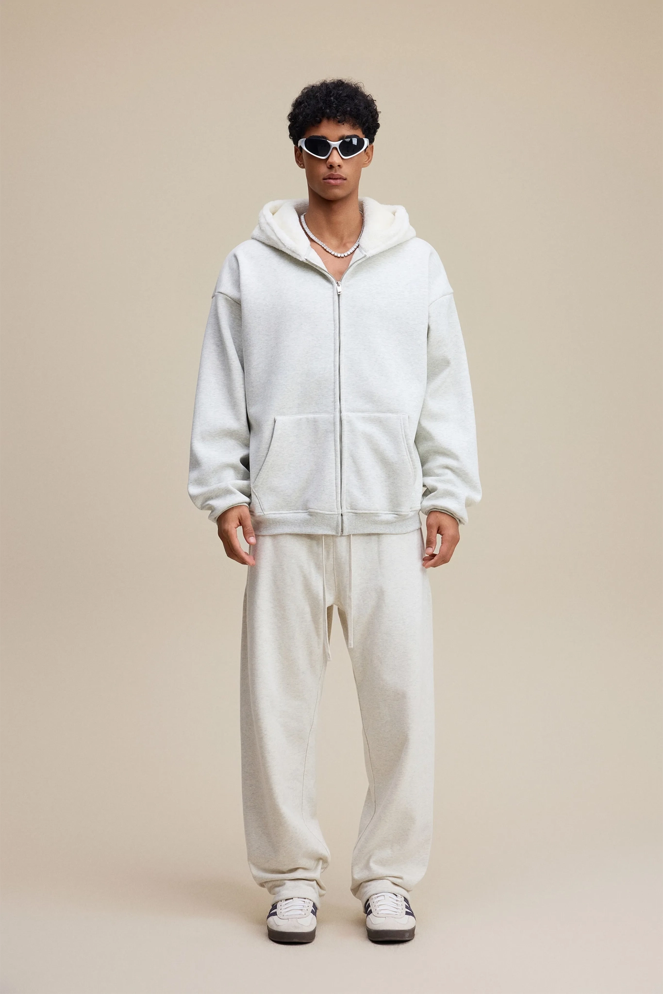 Person wearing a white hoodie and pants set on a beige background