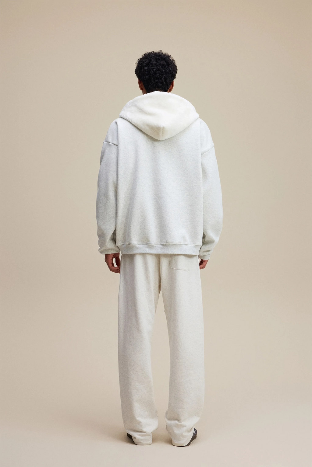 Person wearing a light gray hoodie and pants on a beige background