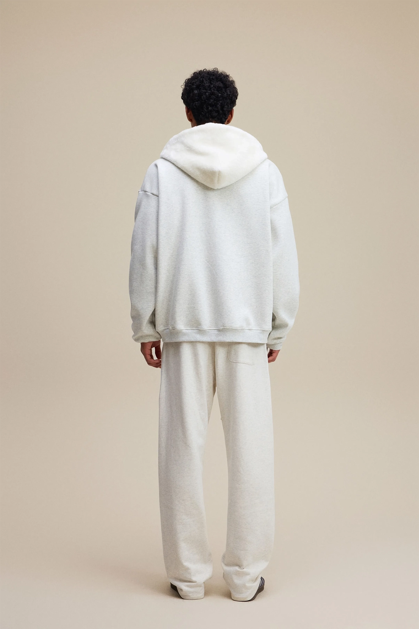 Person wearing a light gray hoodie and pants on a beige background