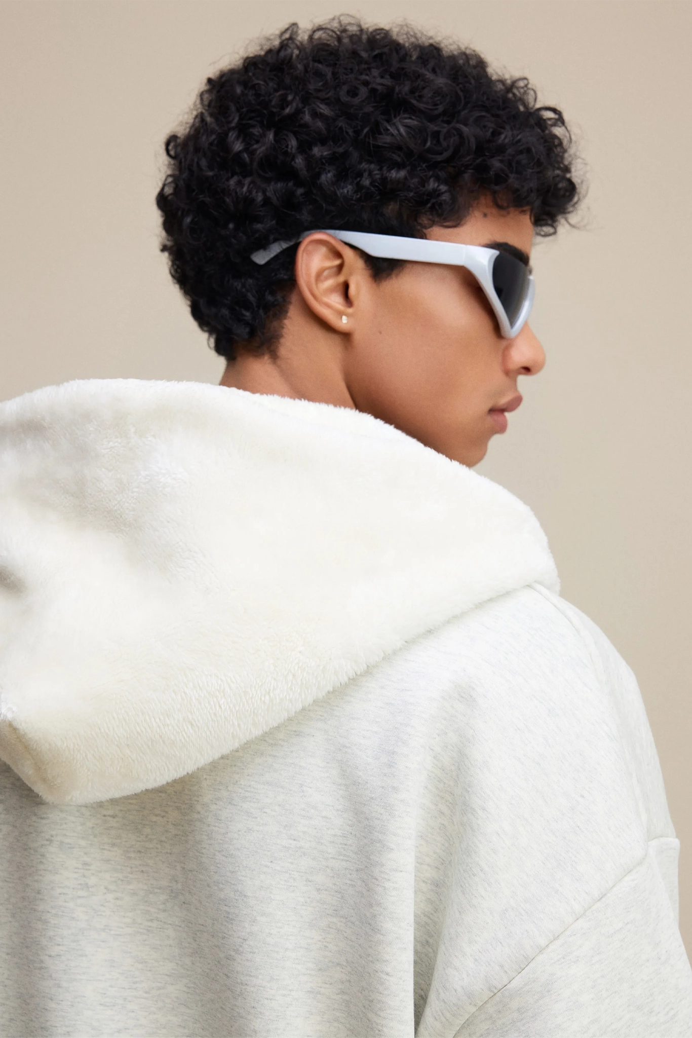 Person wearing a white hoodie and sunglasses with a neutral background