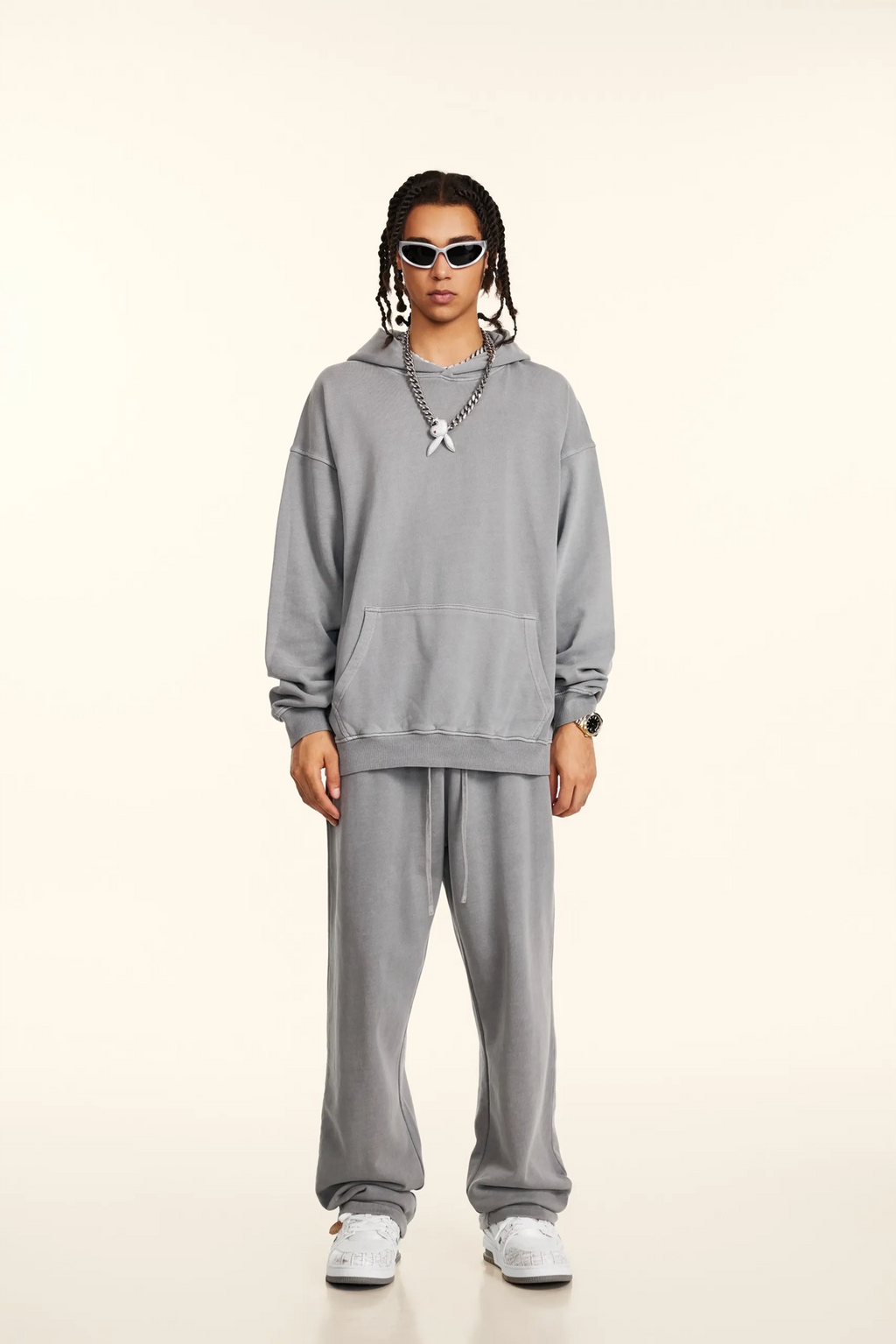 Person wearing a gray tracksuit with sunglasses on a white background