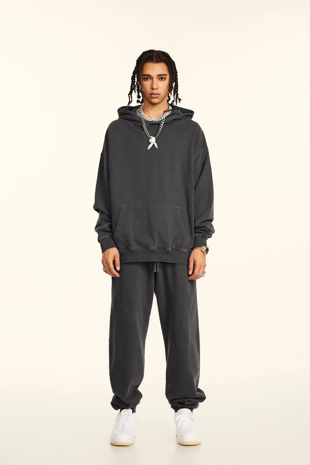 Person wearing a dark gray hoodie and pants on a beige background