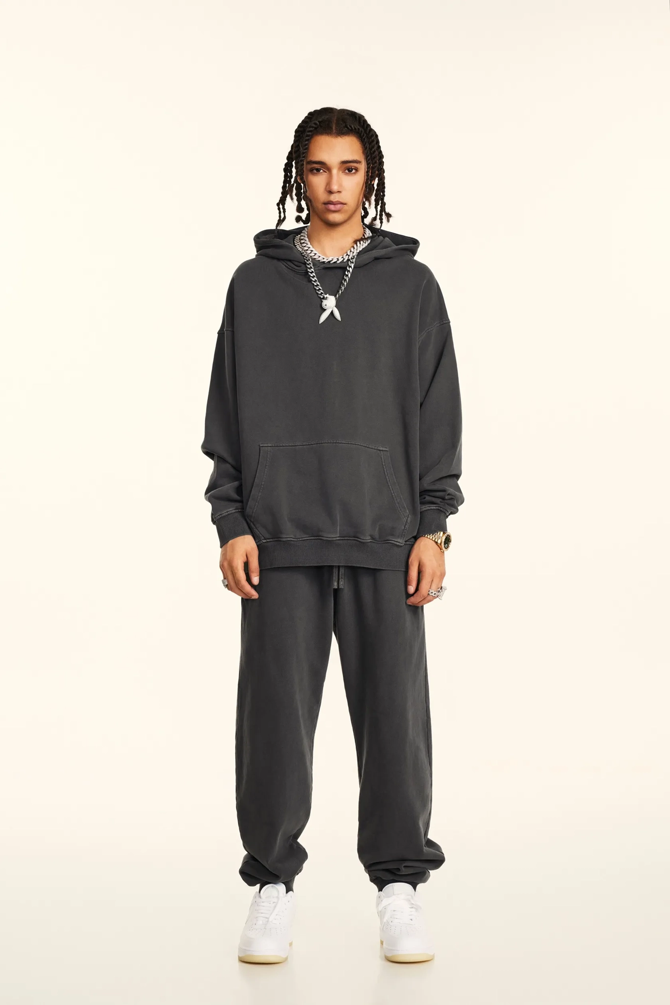 Person wearing a dark gray hoodie and pants on a beige background