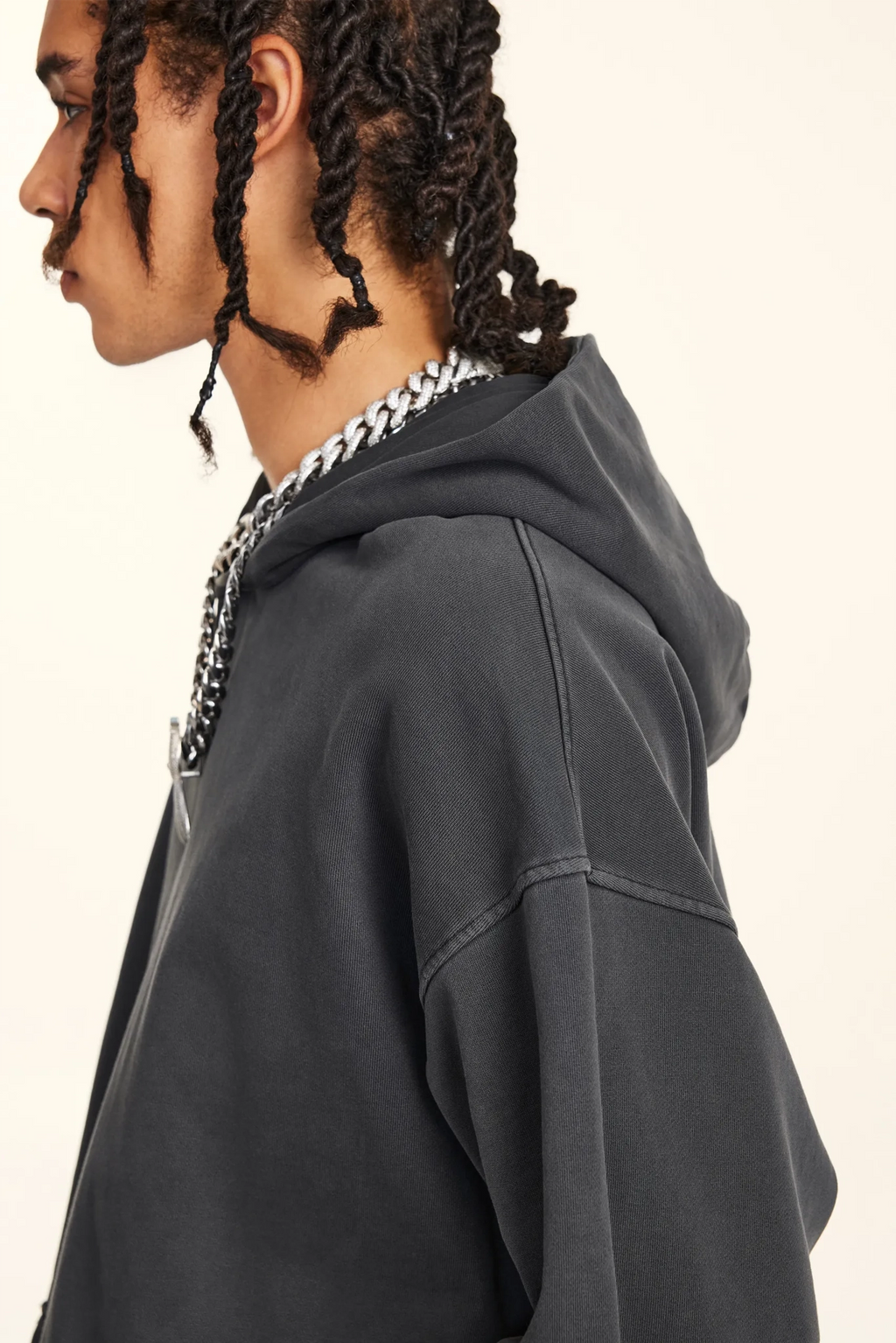 Person wearing a dark gray hoodie with a chain necklace on a plain background