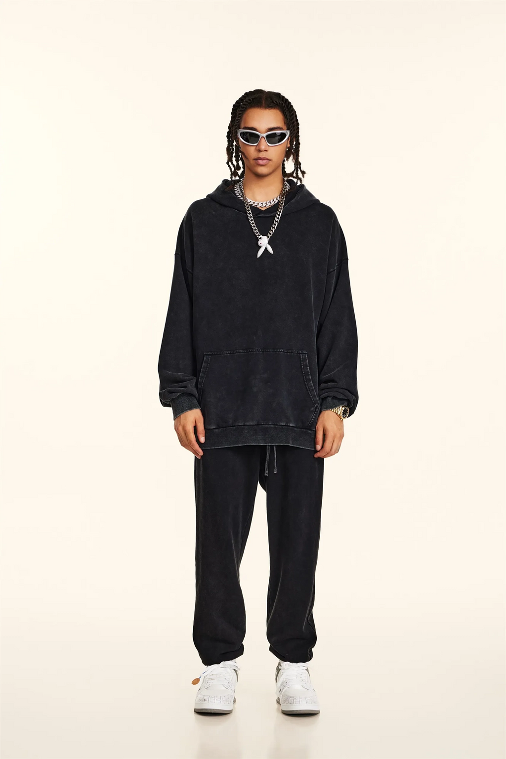 Person wearing a black hoodie and pants with white sneakers on a beige background