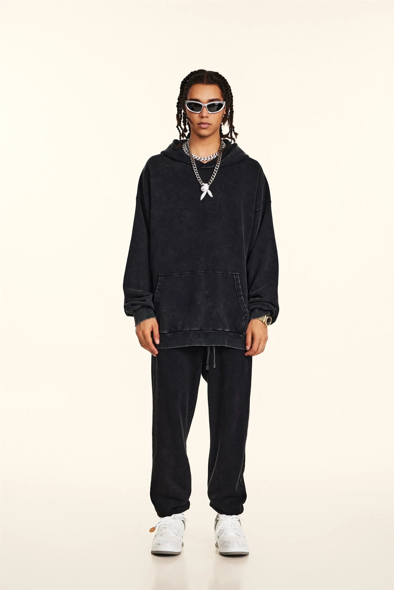 Person wearing a black hoodie and pants with white sneakers on a beige background