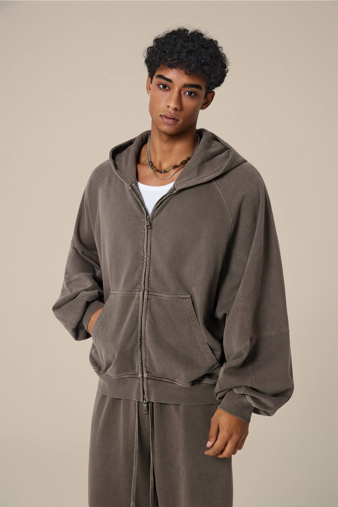 Person wearing a brown hoodie and pants against a beige background