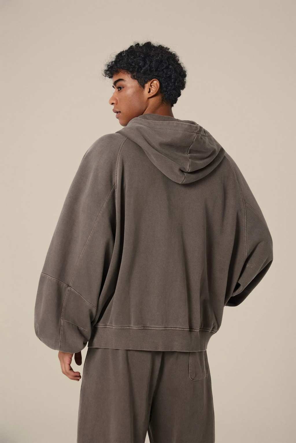 Person wearing a brown hoodie and pants on a beige background