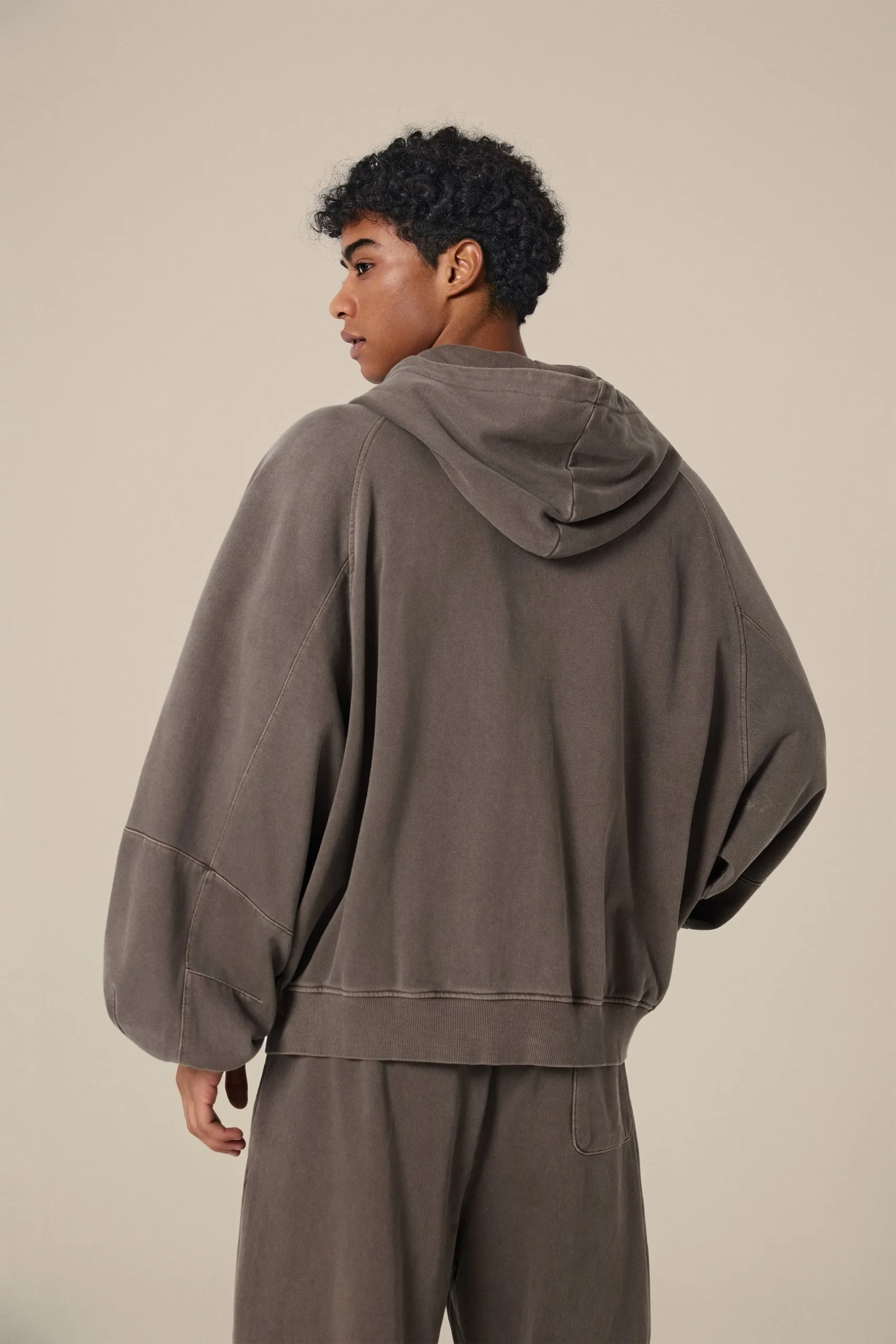 Person wearing a brown hoodie and pants on a beige background