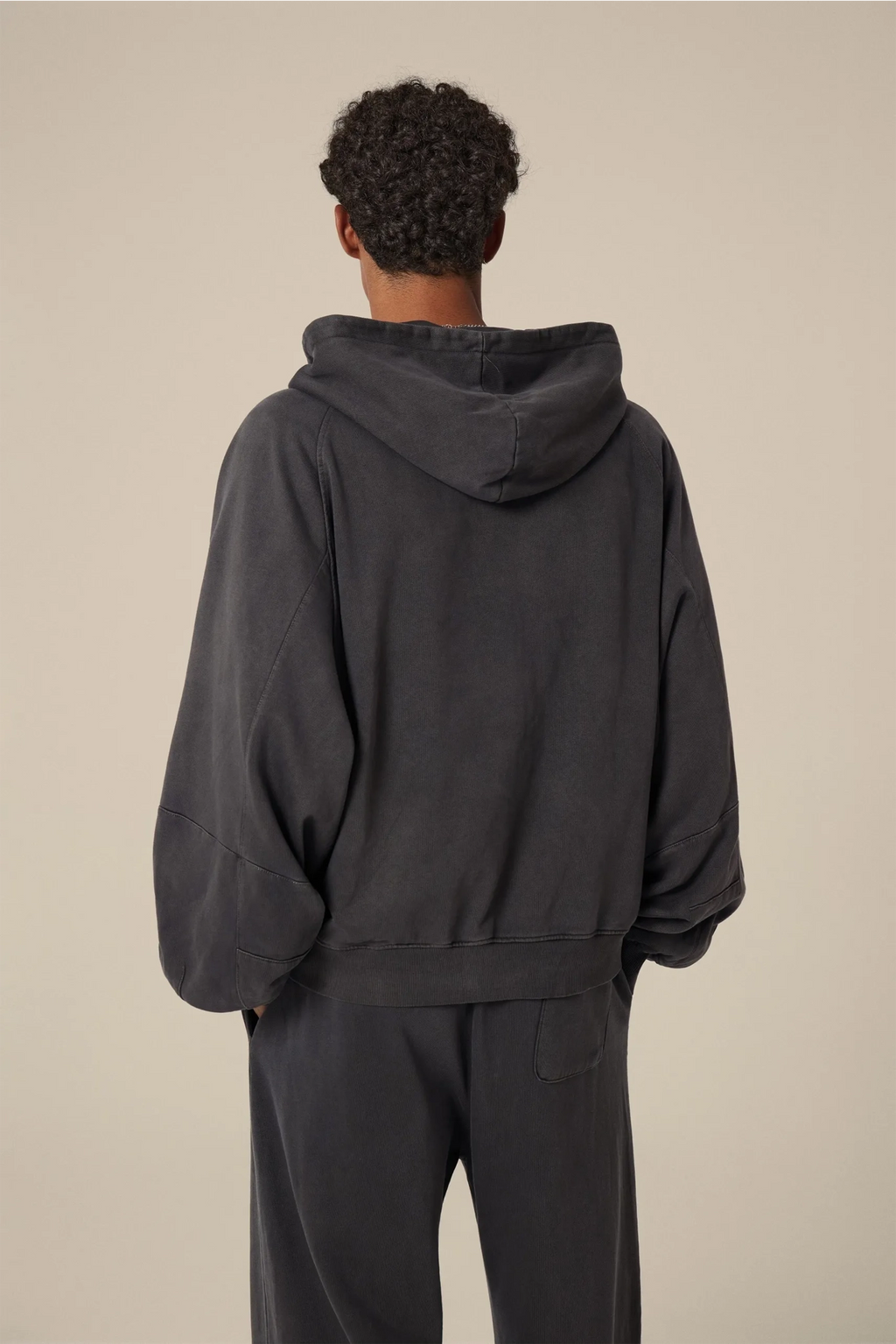 Person wearing a dark gray hoodie and pants on a beige background
