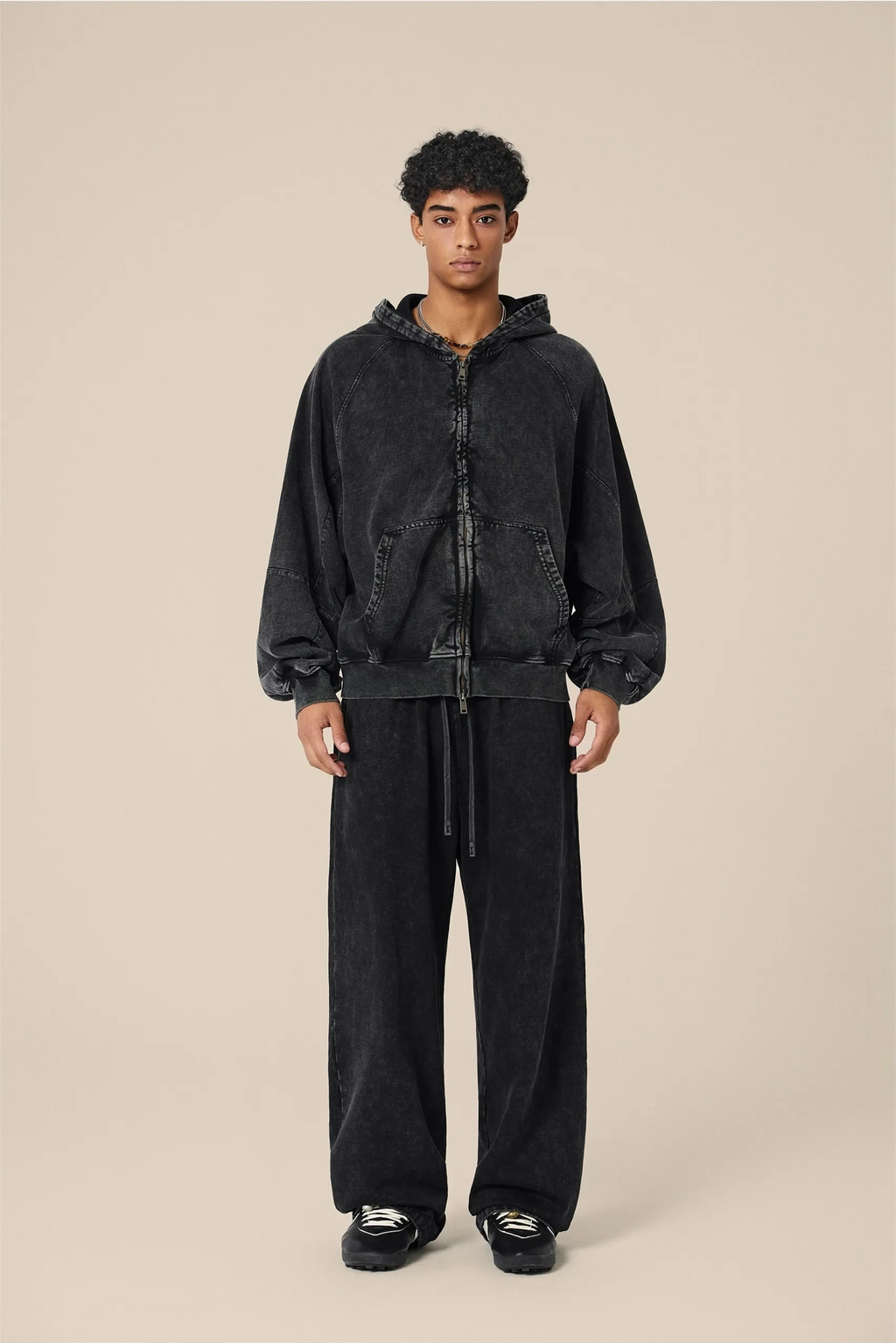 Person wearing a black hoodie and pants on a beige background