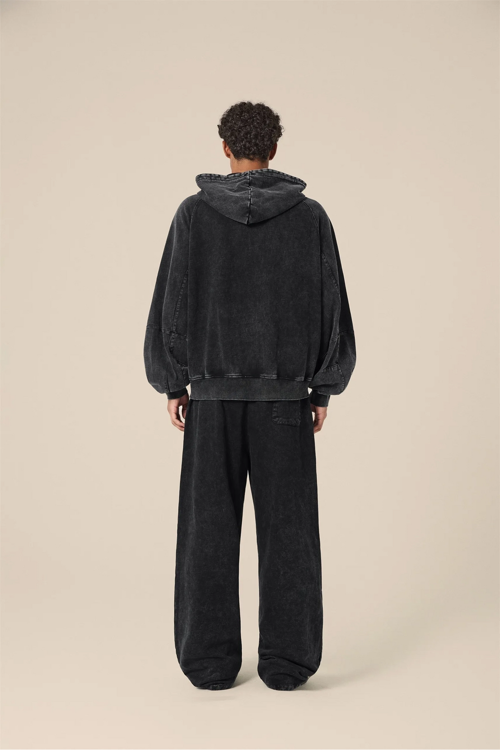 Person wearing a black hoodie and pants on a beige background