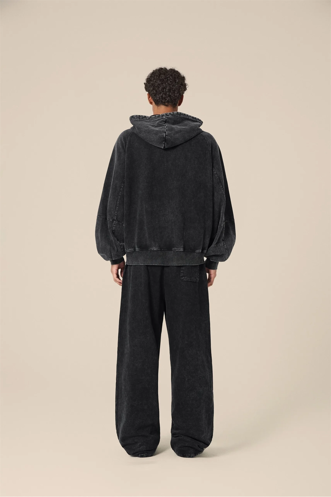 Person wearing a black hoodie and pants on a beige background