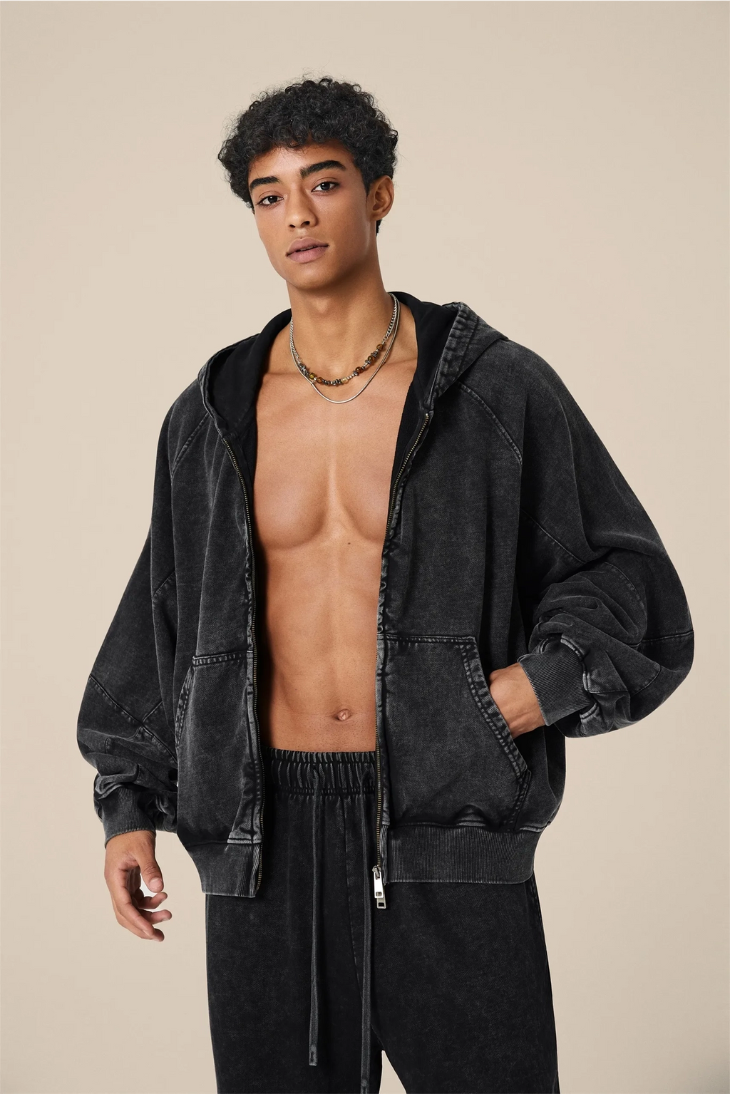 Man wearing a black hoodie without a shirt on a beige background