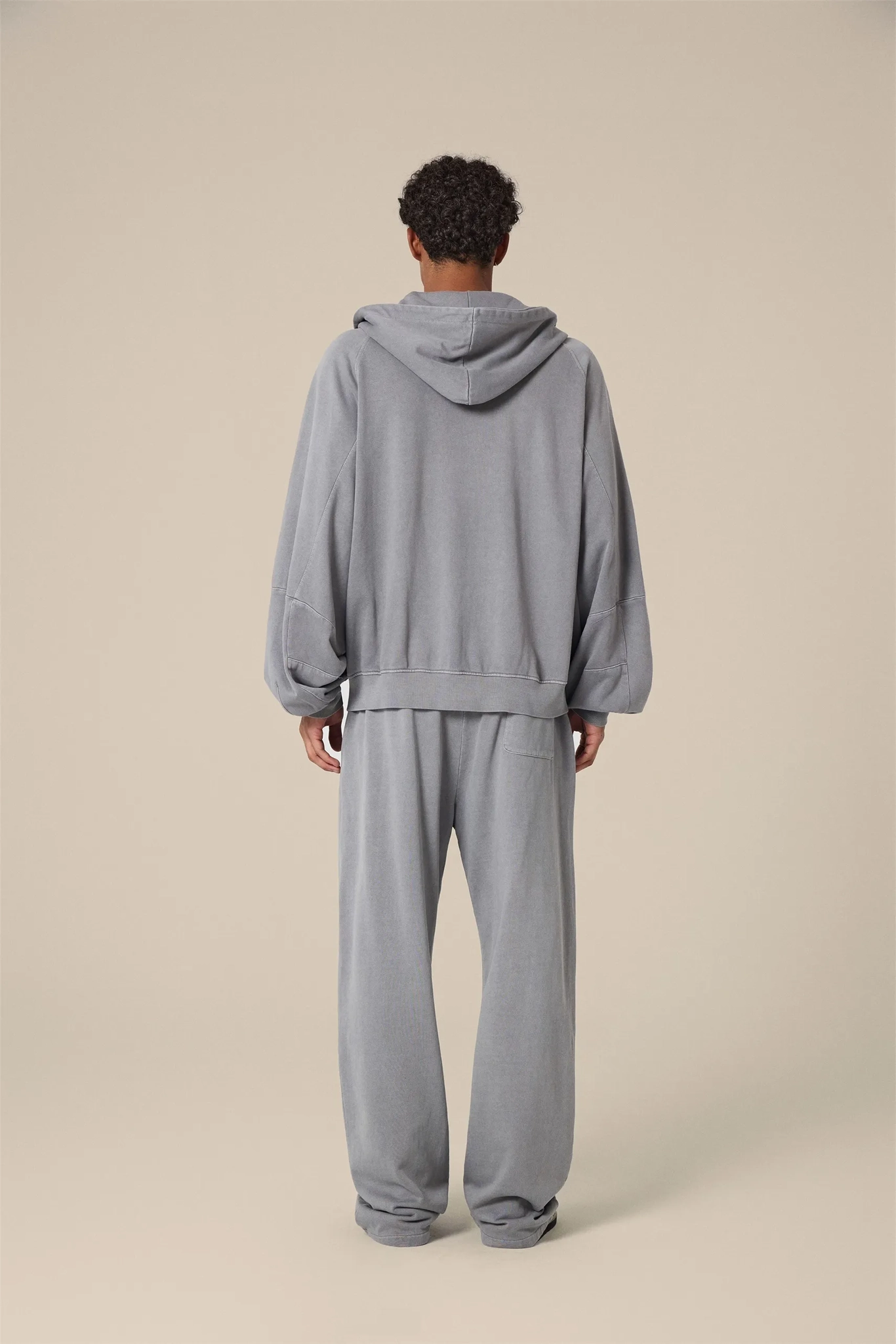 Person wearing a gray tracksuit standing against a beige background