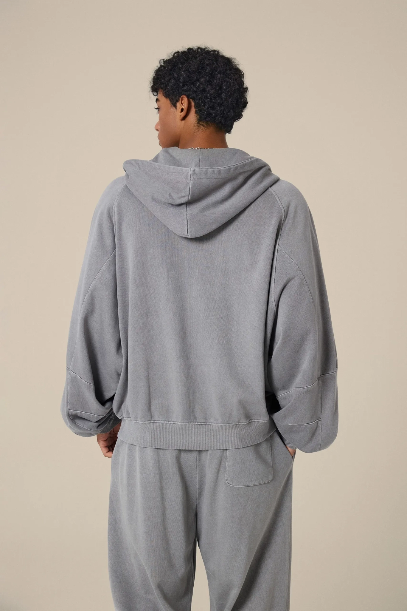 Person wearing a gray hoodie and pants set on a beige background