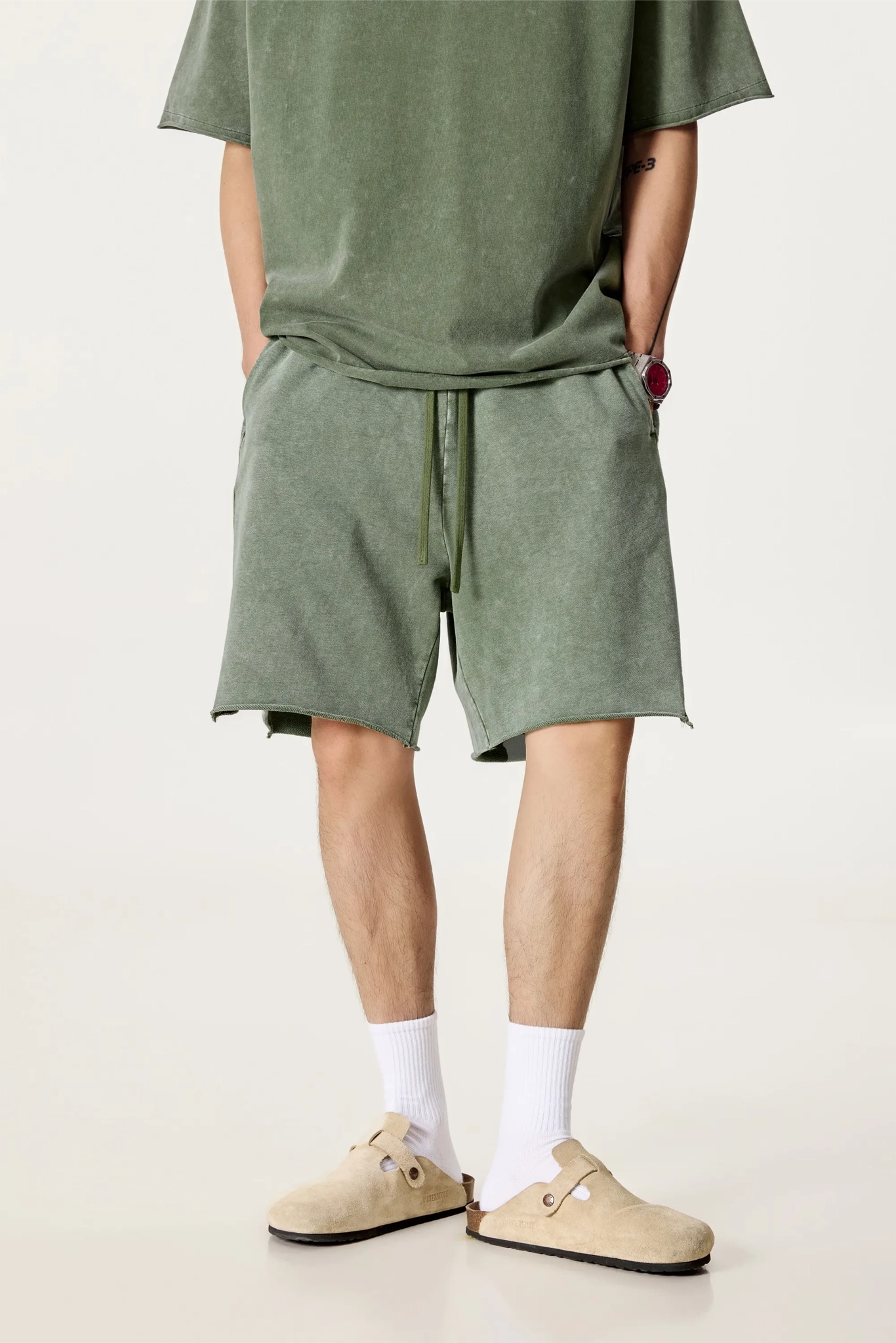 Person wearing a green t-shirt and shorts with beige shoes on a light background