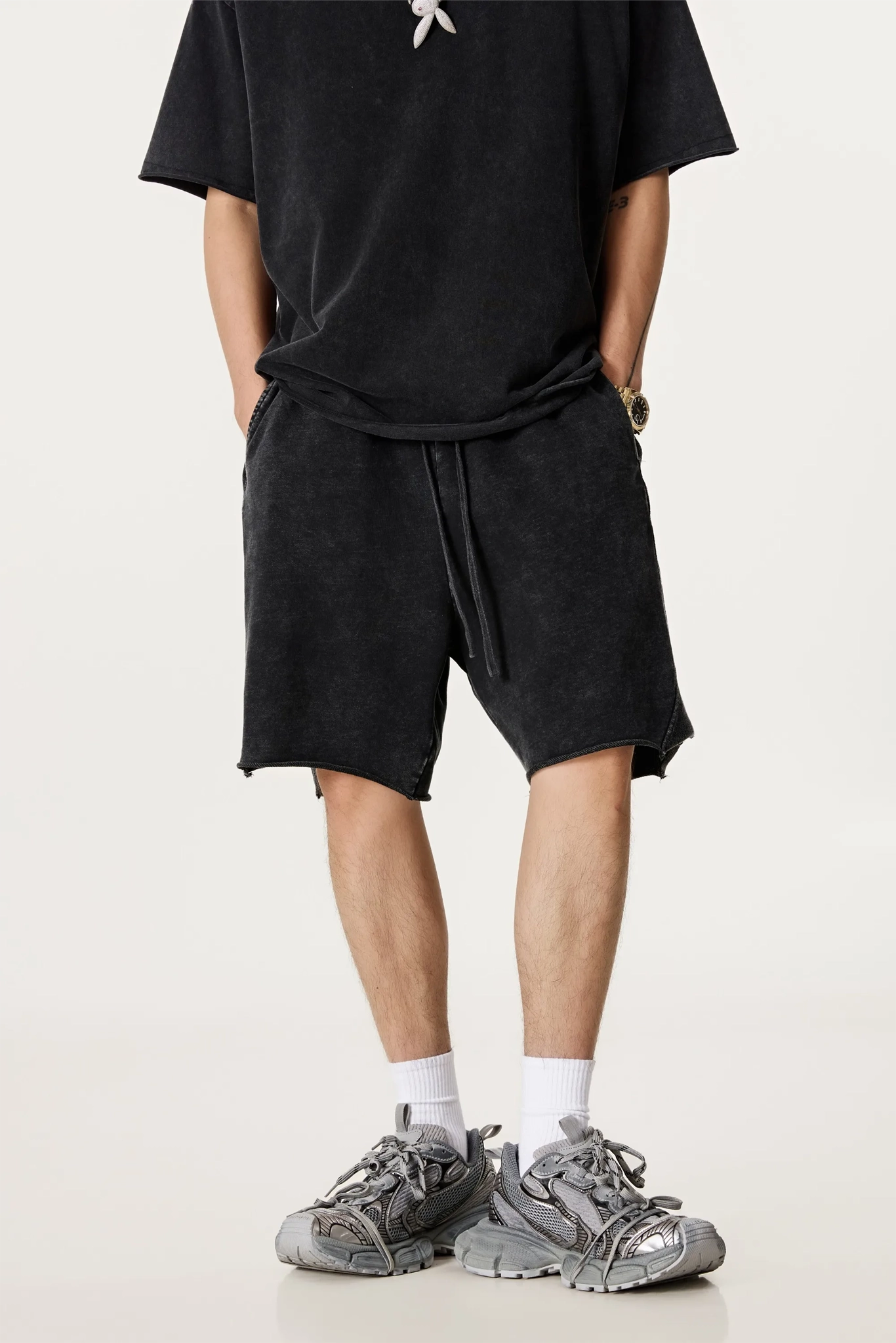 Person wearing a black t-shirt and shorts with gray sneakers on a white background
