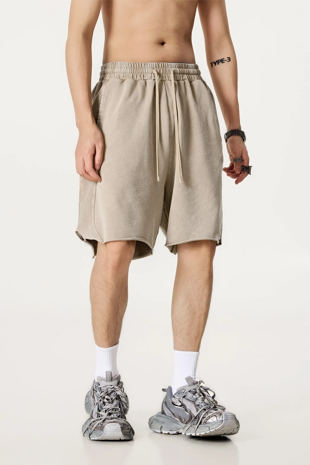 Person wearing beige shorts and gray sneakers on a plain background