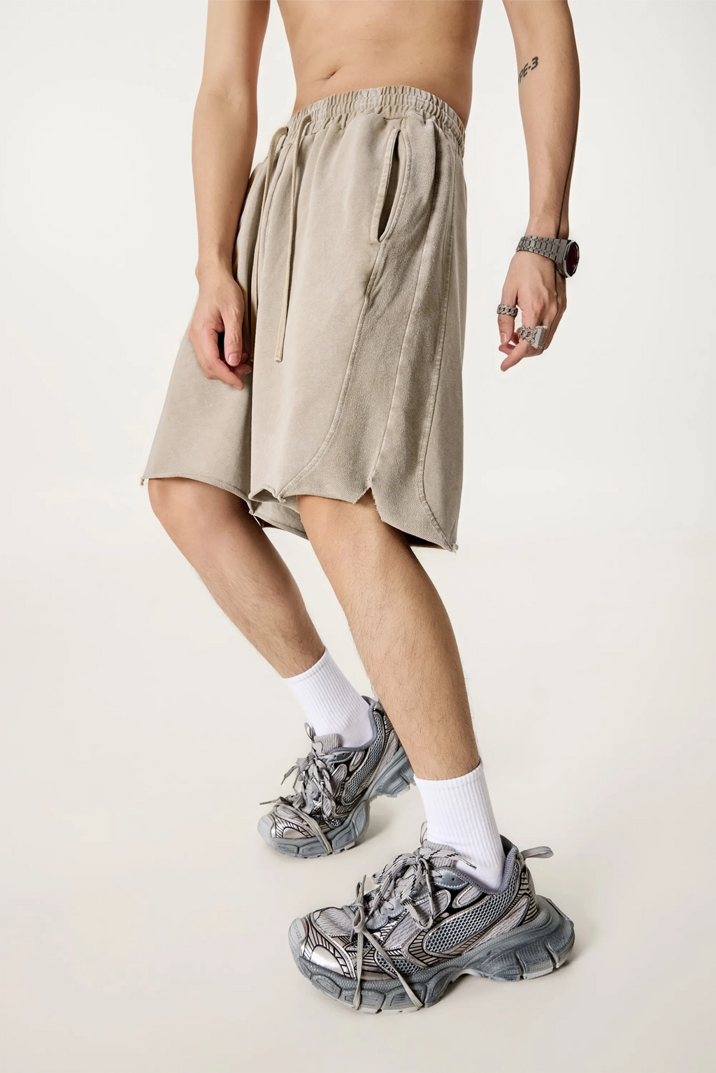 Person wearing beige shorts and white socks with gray sneakers on a plain background