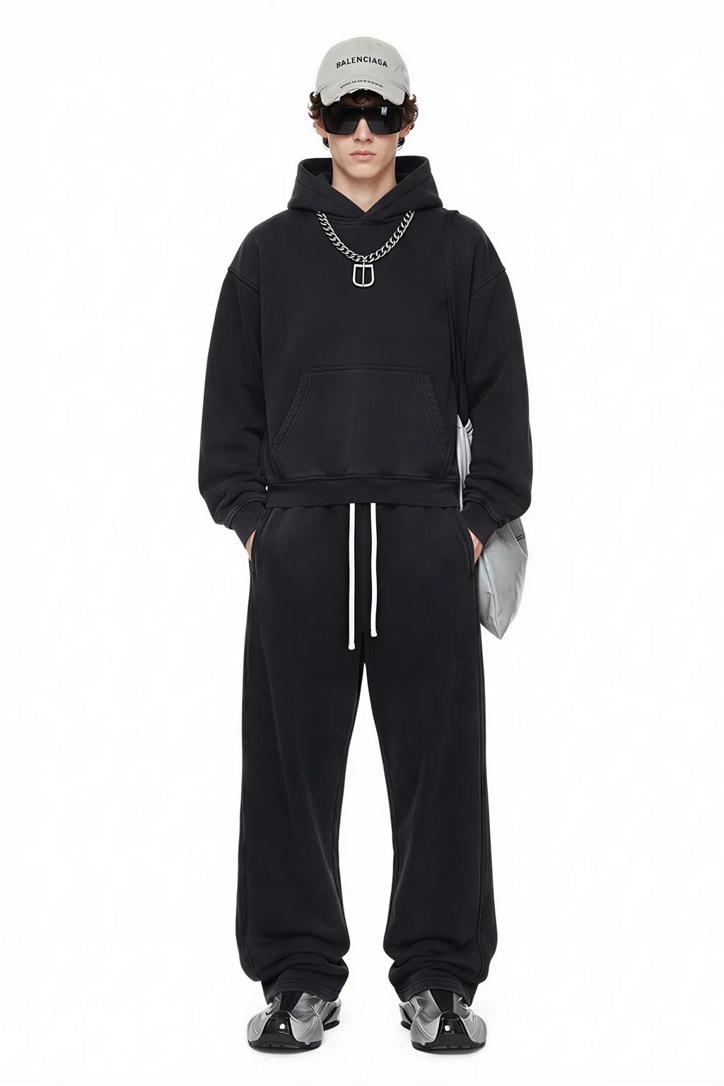 Person wearing a black hoodie and pants with a white cap and sunglasses on a white background