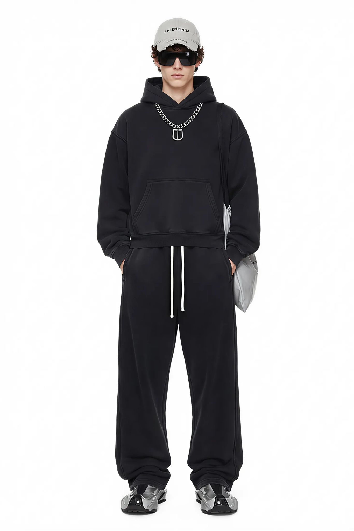 Person wearing a black hoodie and pants with a white cap and sunglasses on a white background