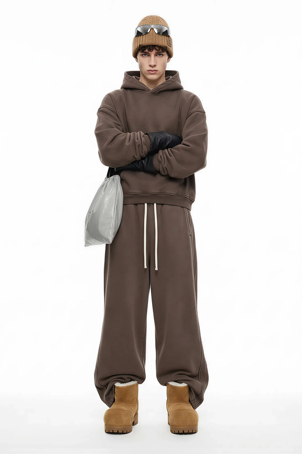 Person wearing a brown hoodie, pants, and boots with a beanie and sunglasses on a white background