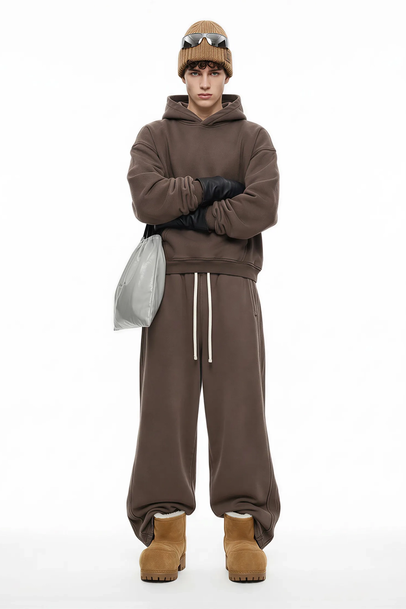 Person wearing a brown hoodie, pants, and boots with a beanie and sunglasses on a white background