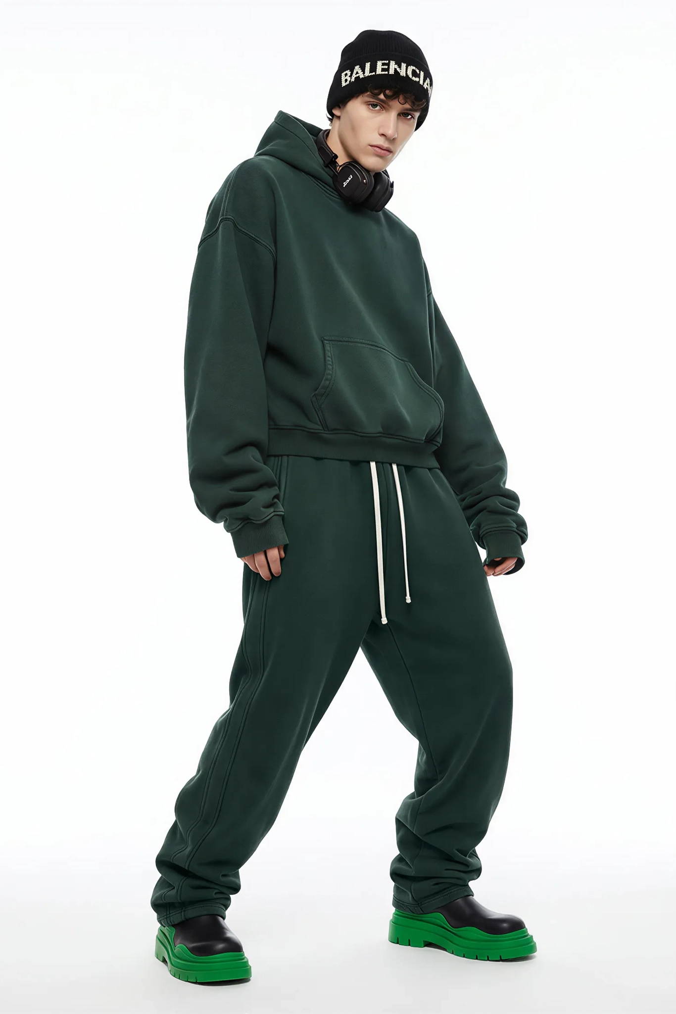 Person wearing a green tracksuit with Balenciaga cap on a white background