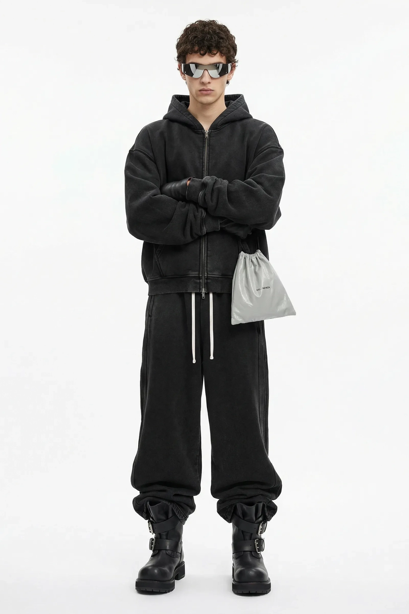 Person wearing a black outfit with sunglasses and a white bag on a white background
