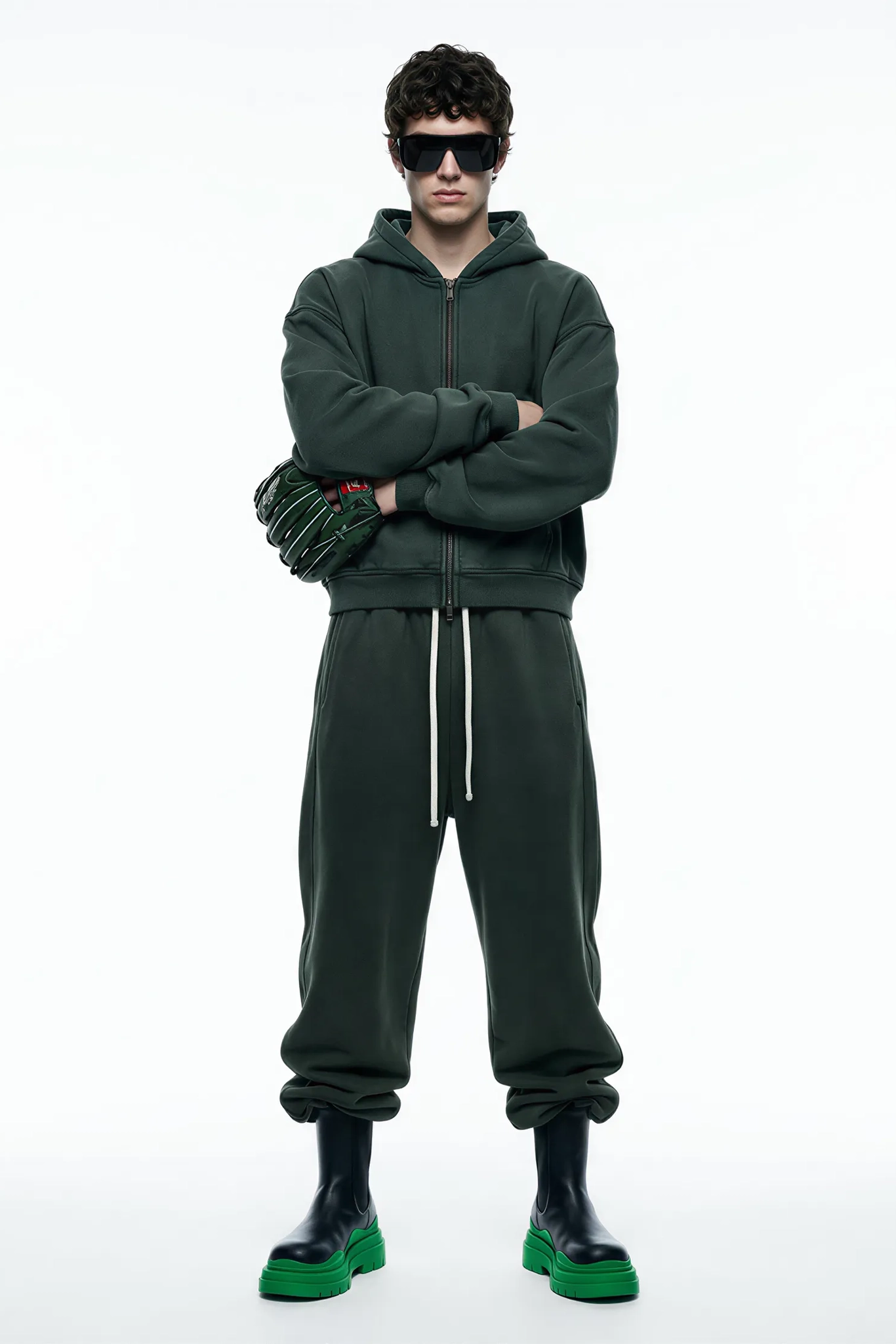 Person wearing a green tracksuit with sunglasses on a white background