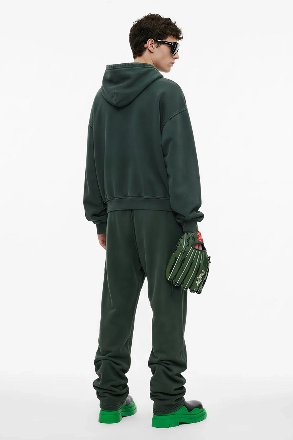 Person wearing a green tracksuit holding green gloves on a white background