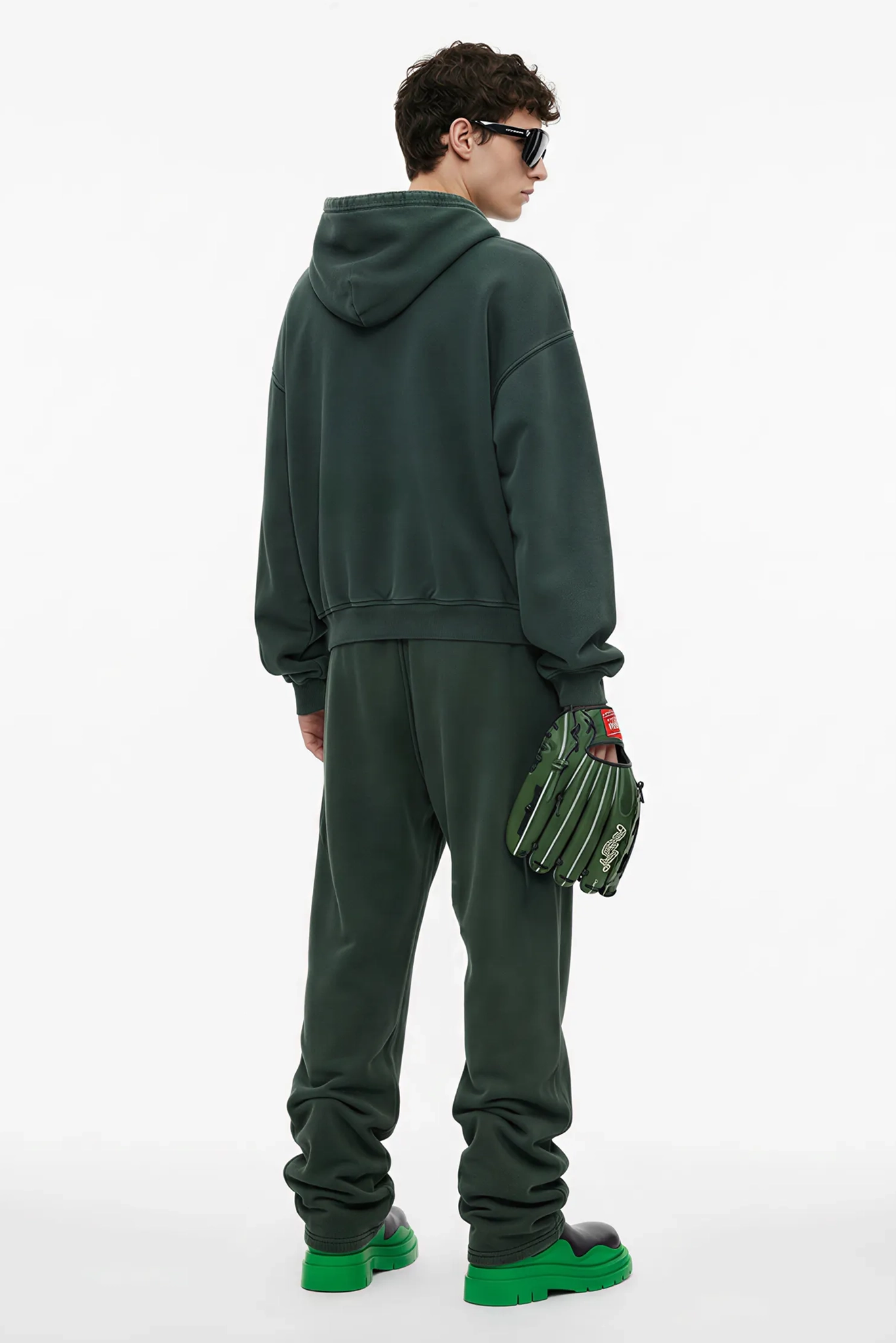 Person wearing a green tracksuit holding green gloves on a white background