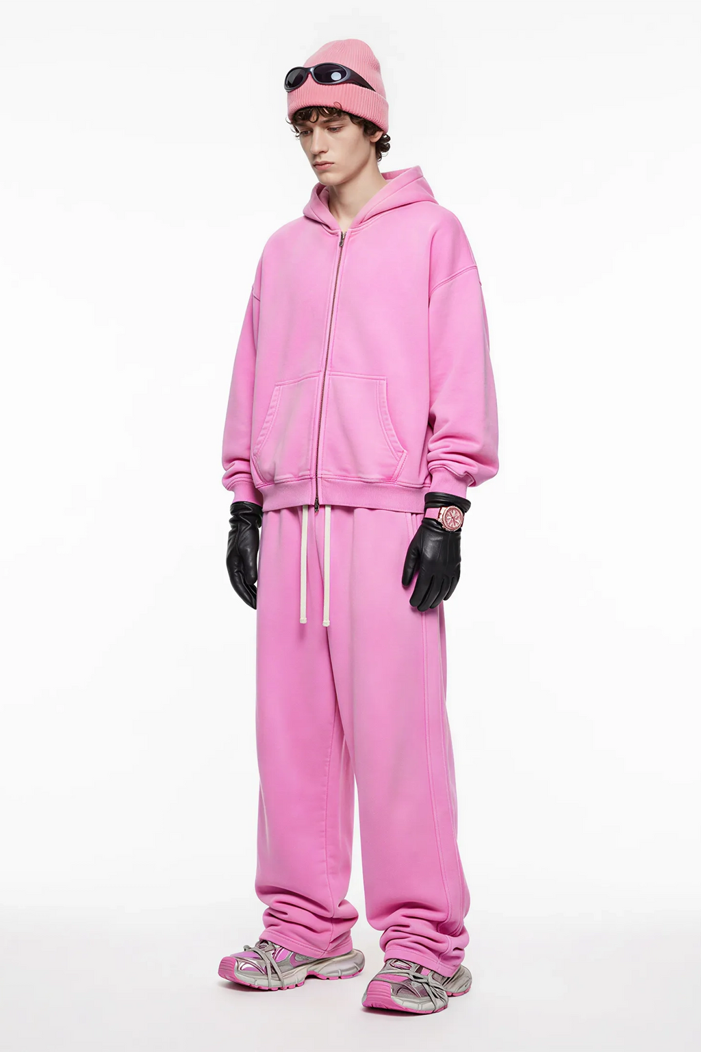 Person wearing a pink tracksuit with matching hat and gloves on a white background