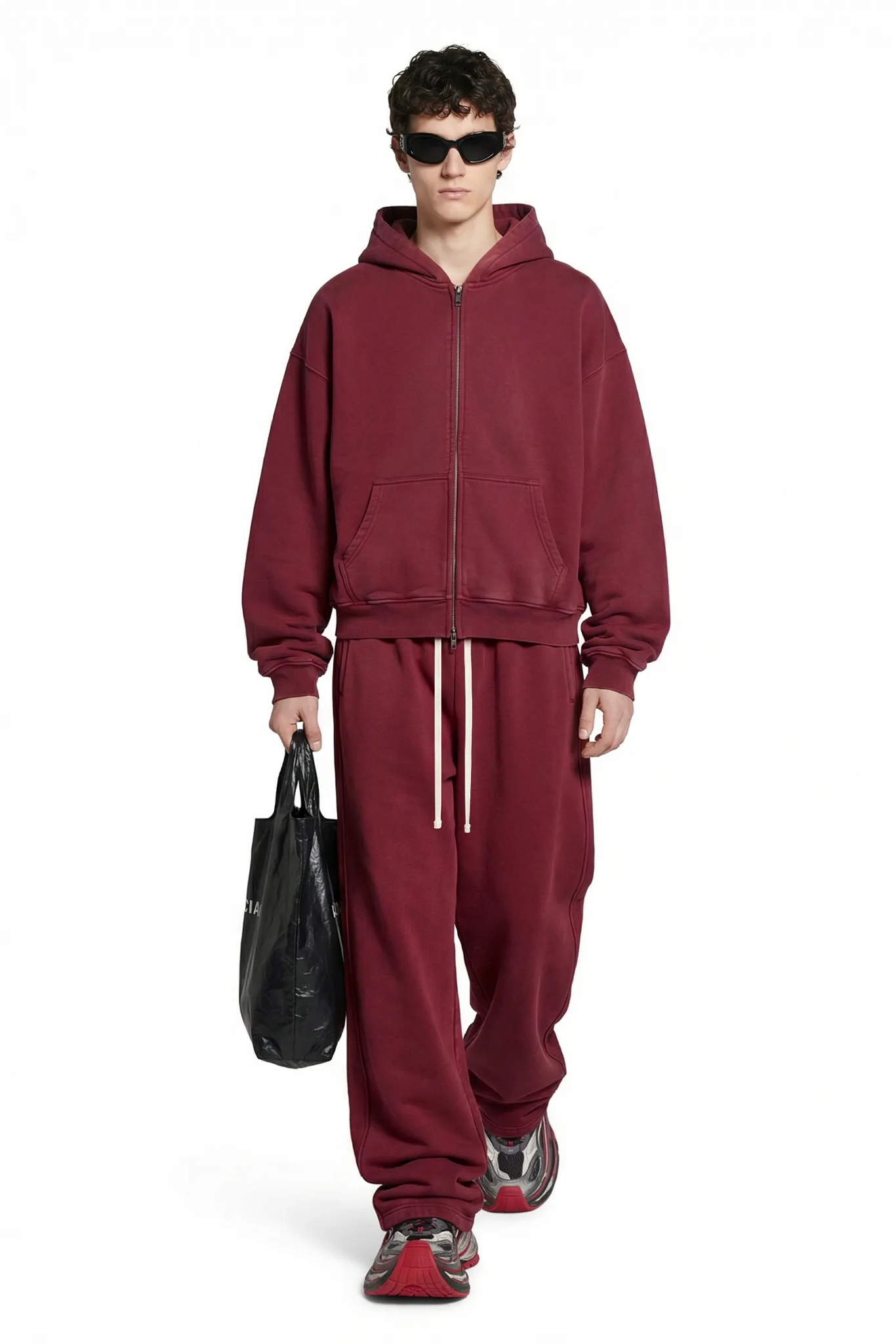 Person wearing a maroon tracksuit holding a black bag on a white background