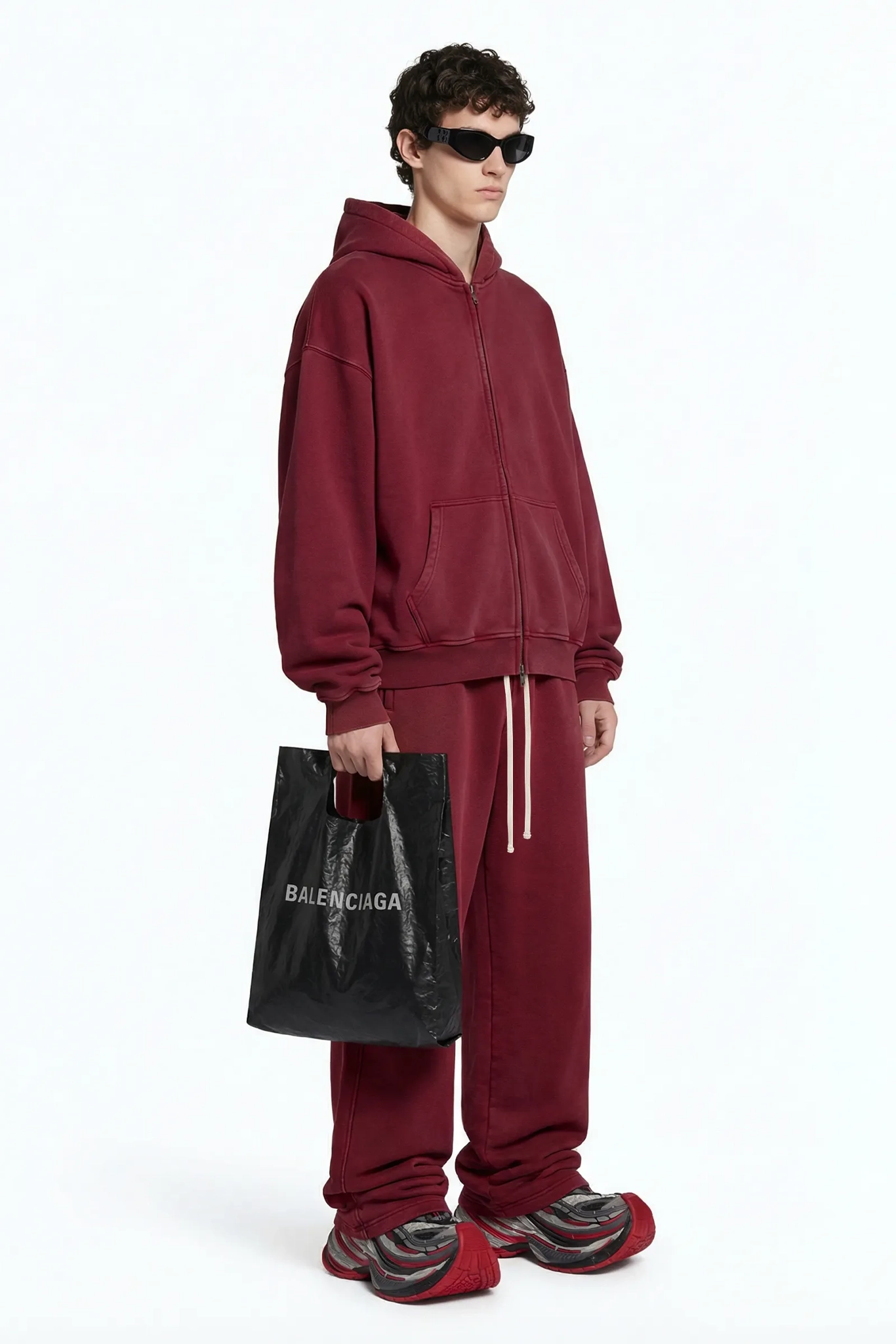 Person wearing a red tracksuit holding a Balenciaga bag on a white background