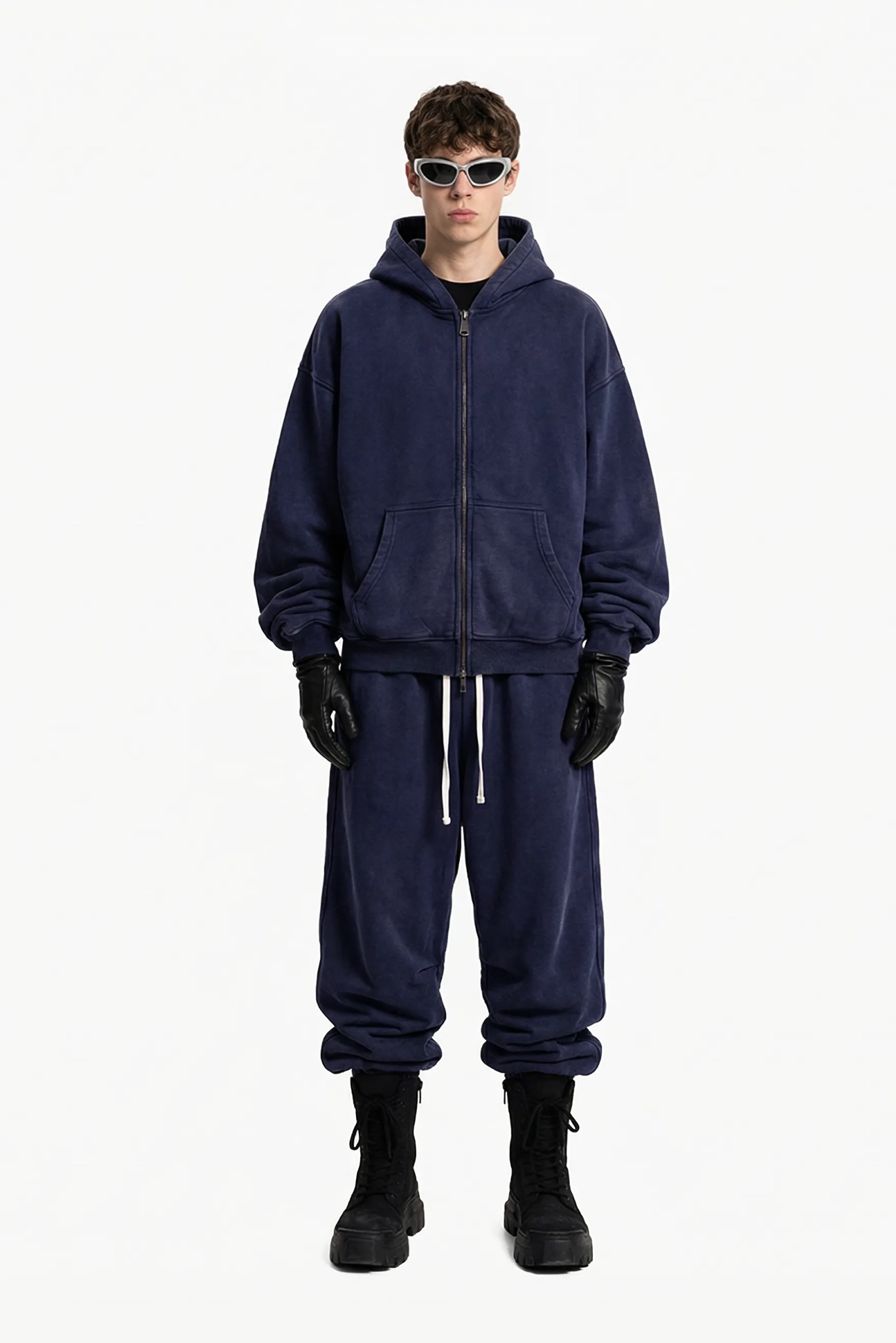 Person wearing a navy blue tracksuit with black gloves and boots on a white background