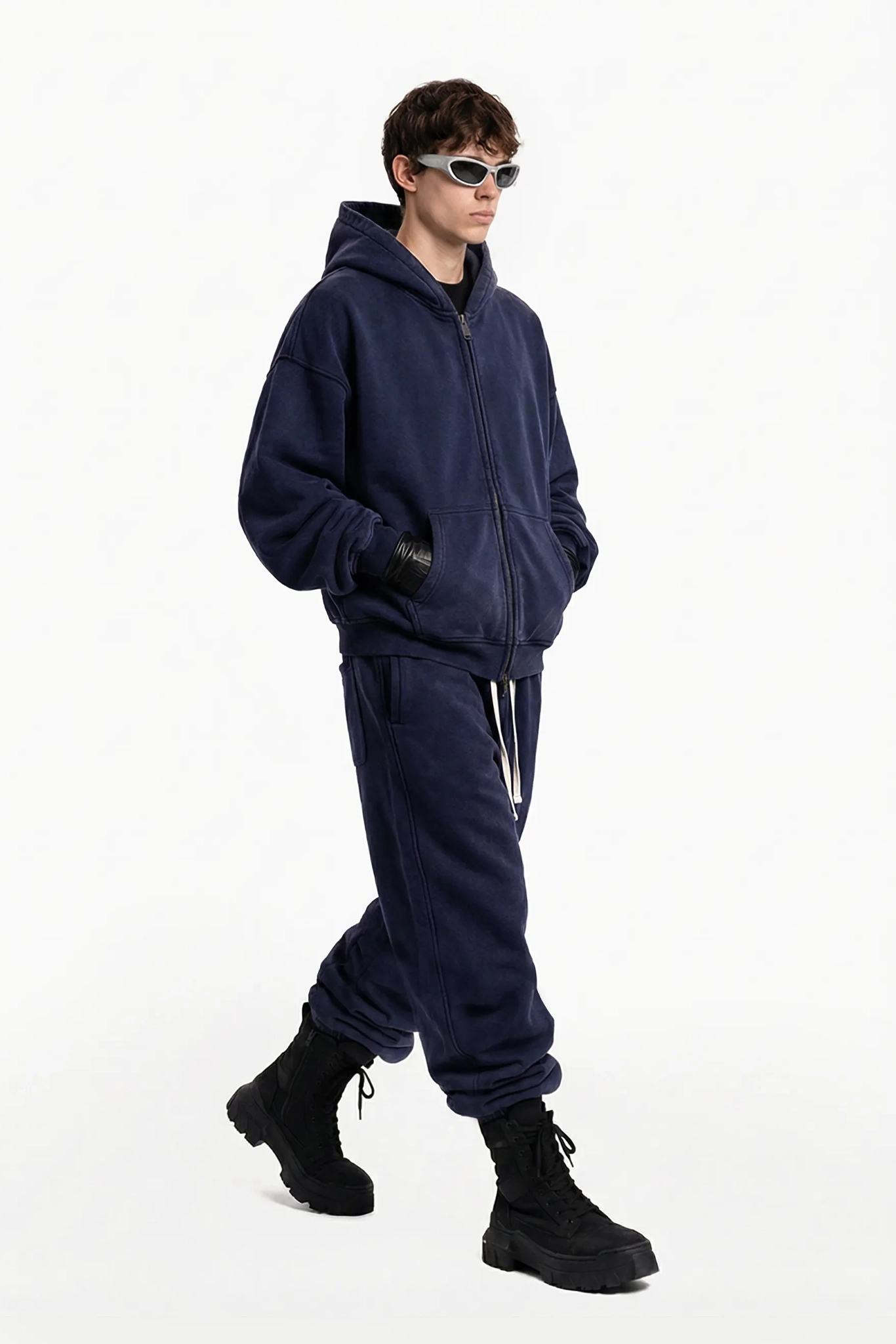 Person wearing a navy blue tracksuit and black boots on a white background