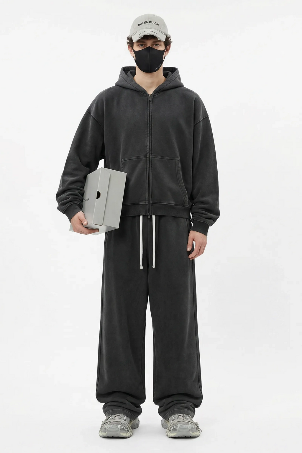 Person wearing a dark gray hoodie and pants holding a laptop on a white background