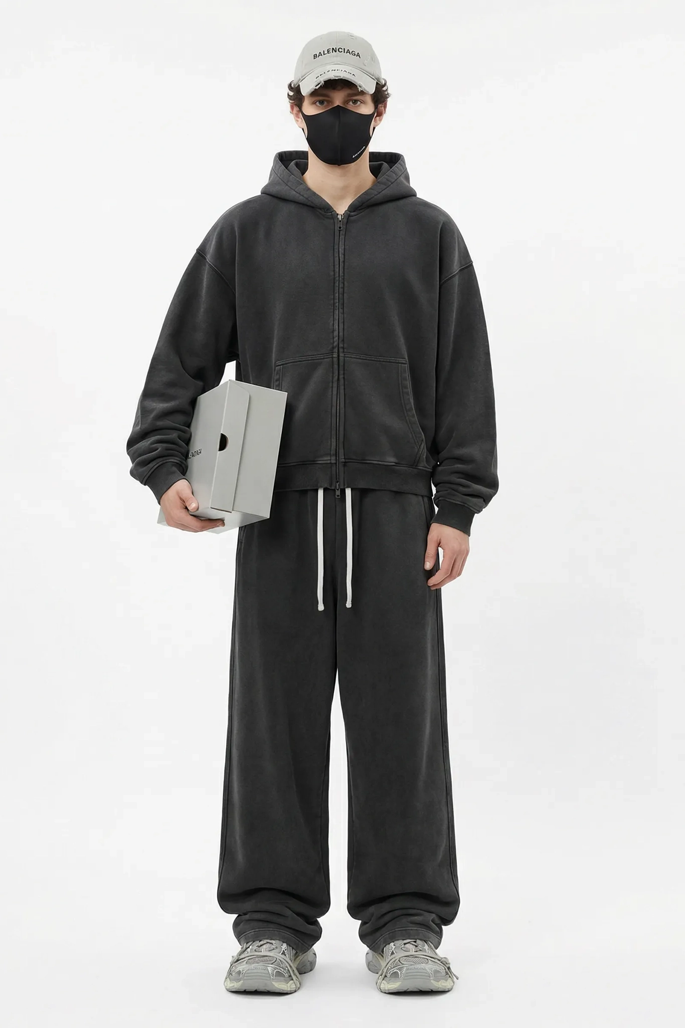 Person wearing a dark gray hoodie and pants holding a laptop on a white background