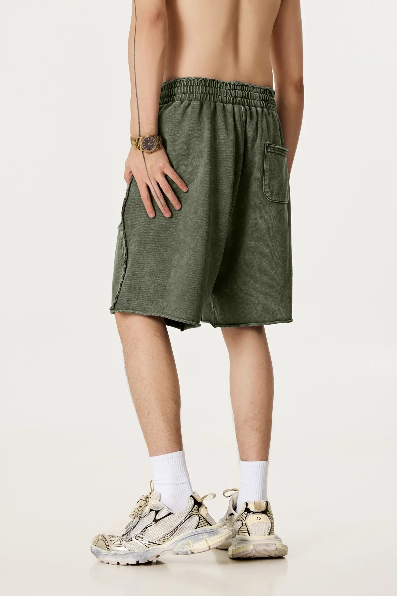 Person wearing green shorts and white sneakers on a plain background