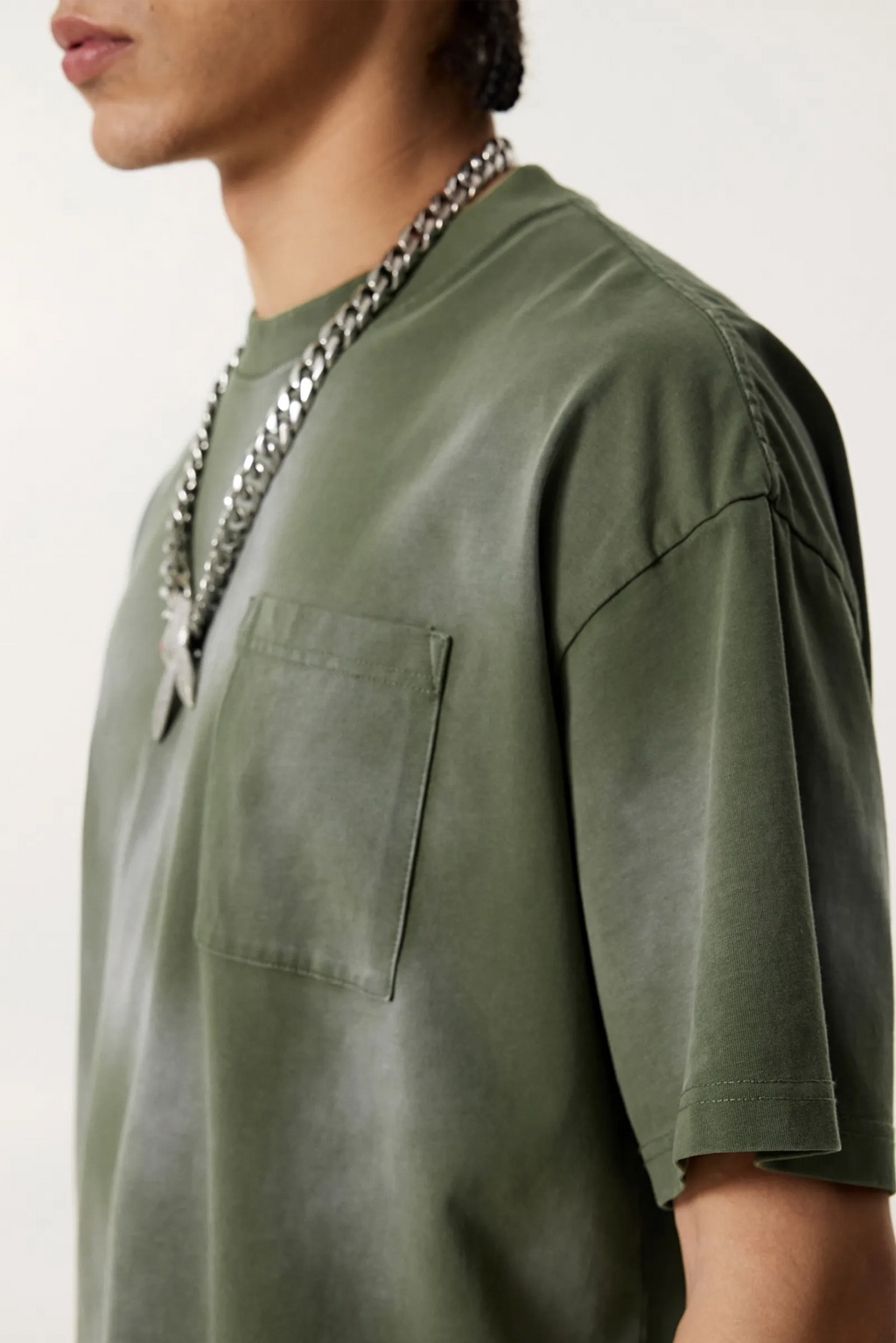 Person wearing a green shirt with a chain necklace on a white background