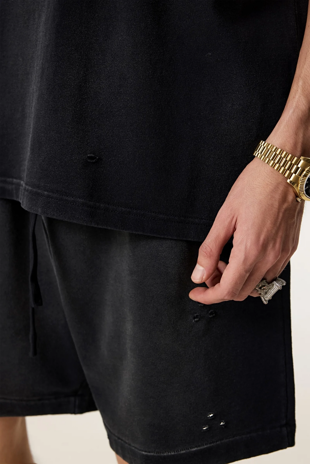 Person wearing a black t-shirt and shorts with a gold watch on a neutral background
