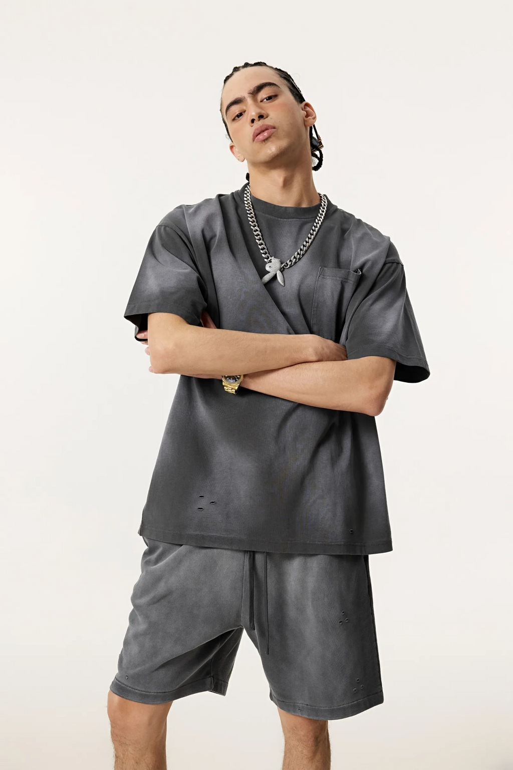 Person wearing a gray outfit with a necklace on a plain background