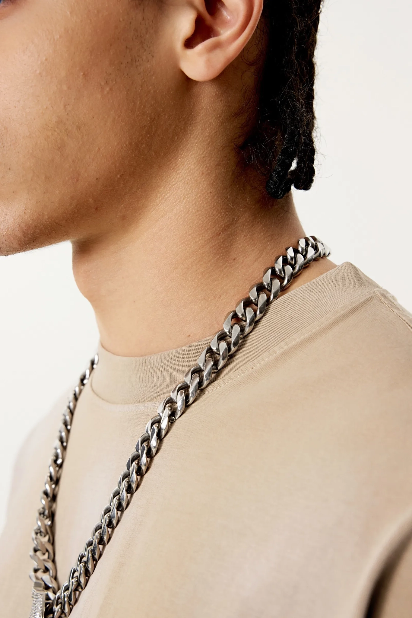Close-up of a person wearing a chain necklace against a neutral background