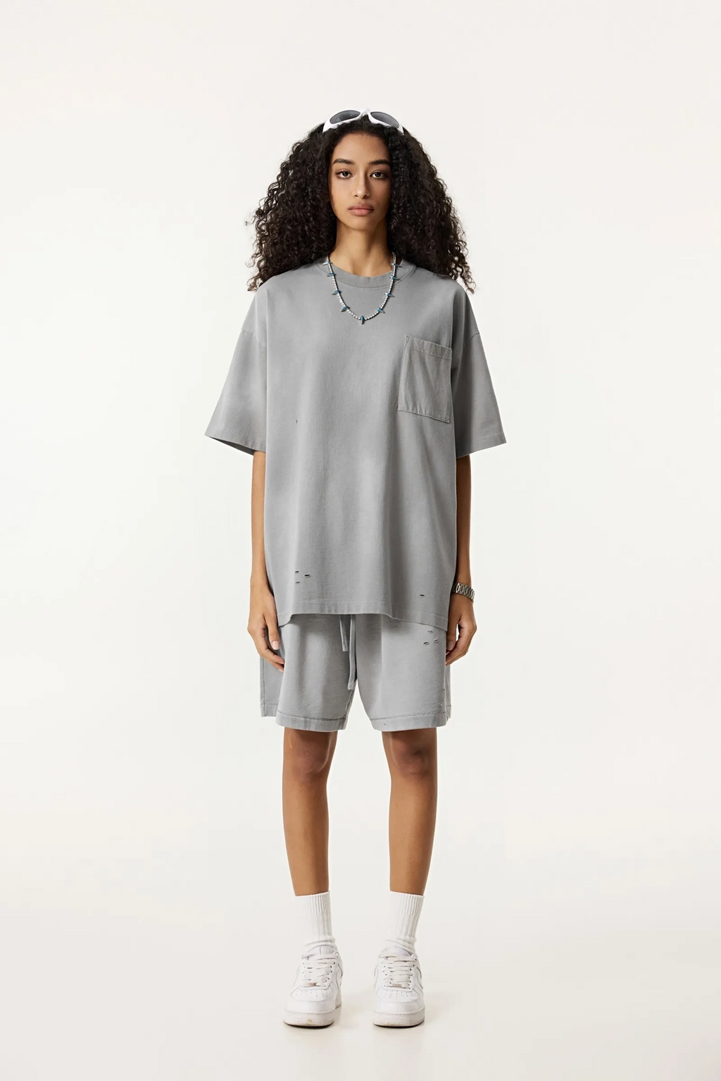 Person wearing a gray oversized t-shirt and shorts set on a white background