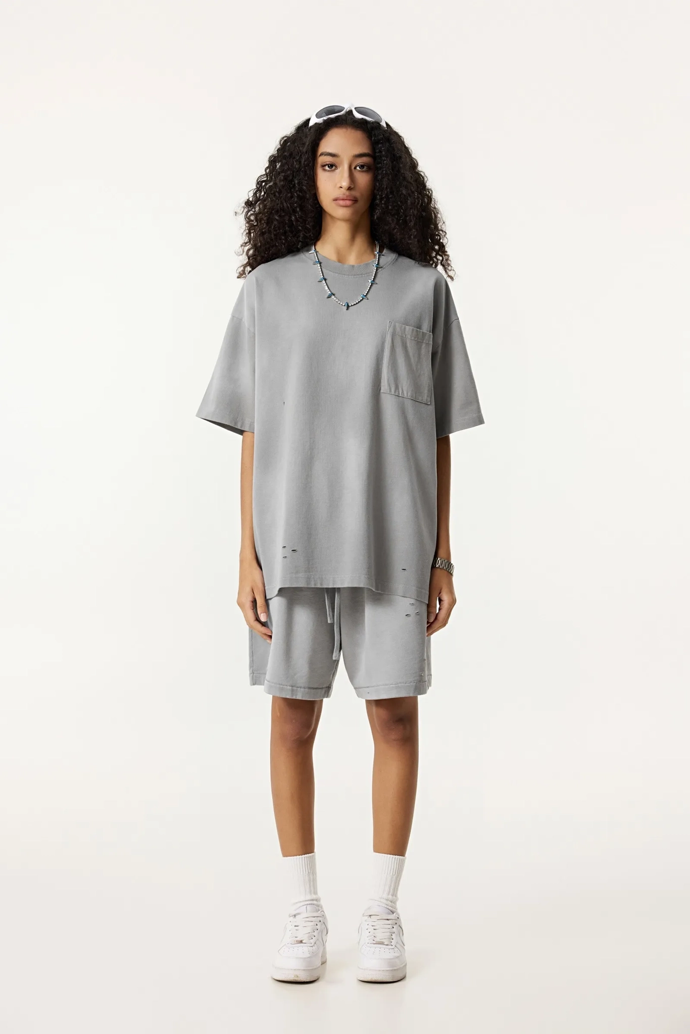 Person wearing a gray oversized t-shirt and shorts set on a white background