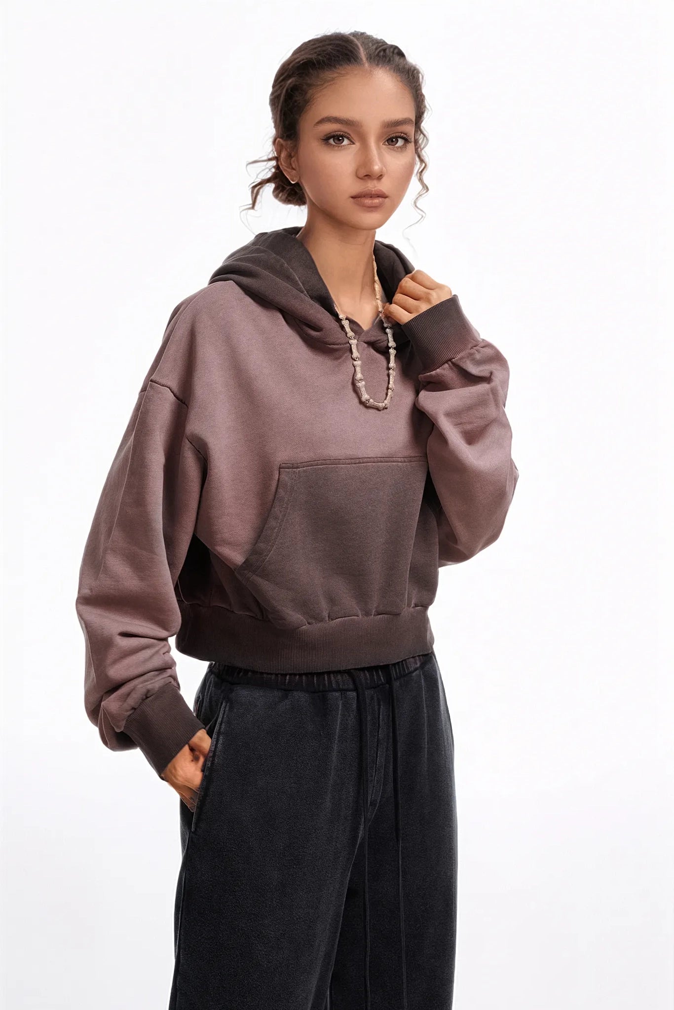 Person wearing a brown hoodie and black pants on a white background